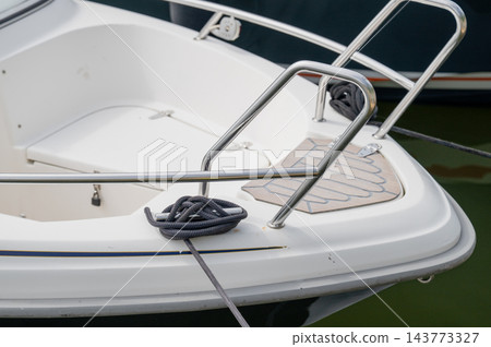 White motorboat stern with stainless steel railing and mooring rope in marina water White motorboat stern with stainless steel railing and mooring rope in marina water 143773327