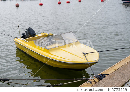 Yellow motorboat moored at marina dock with calm water and nautical harbor background Yellow motorboat moored at marina dock with calm water and nautical harbor background 143773329