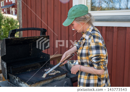 Woman grilling food on outdoor barbecue at summer cottage terrace in Finland 143773543