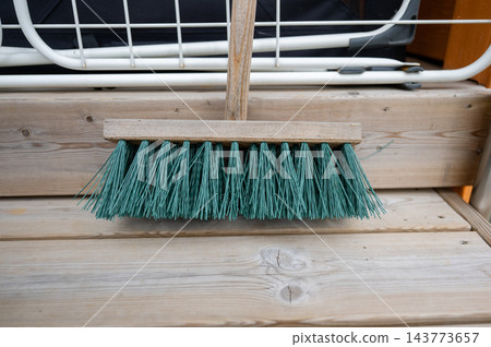Outdoor broom with wooden handle and green bristles on wooden deck near railing Outdoor broom with wooden handle and green bristles on wooden deck near railing 143773657
