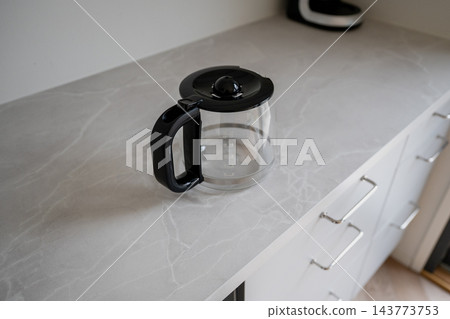 Glass coffee pot with black handle on light kitchen countertop minimalist interior scene Glass coffee pot with black handle on light kitchen countertop minimalist interior scene 143773753