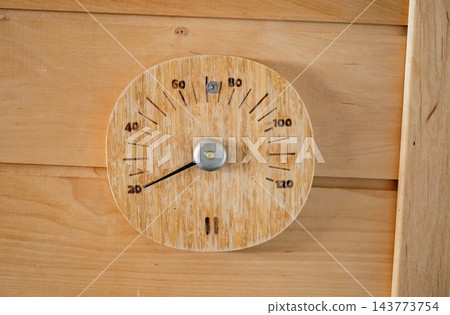 Wooden sauna thermometer on wall showing temperature in rustic interior 143773754