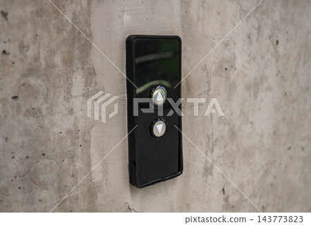 Elevator control panel with up and down buttons on concrete wall, minimal industrial interior detail Elevator control panel with up and down buttons on concrete wall, minimal industrial interior detail 143773823