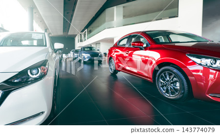 New red and white cars displayed in a modern luxury automobile showroom. Dealership inventory for customers seeking vehicle purchase, leasing, rental and financing. Automotive retail inventory. New red and white cars displayed in a modern luxury automobile showroom. Dealership inventory for customers seeking vehicle purchase, leasing, rental and financing. Automotive retail inventory. 143774079