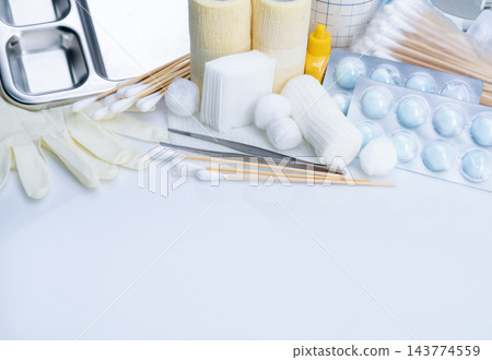 Wound dressing supplies with gauze pads, rolled bandages, cotton balls and wooden swabs beside metal forceps and examination gloves, with a divided tray and individually packaged cotton balls. Wound dressing supplies with gauze pads, rolled bandages, cotton balls and wooden swabs beside metal forceps and examination gloves, with a divided tray and individually packaged cotton balls. 143774559