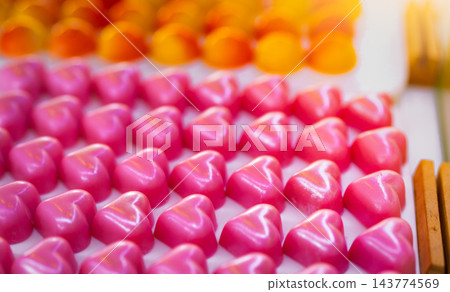 Pink heart shaped chocolate pralines with rose scented white chocolate ganache on a white plate, with yellow and orange dome chocolates nearby, a luxury confectionery assortment for Valentine's Day. Pink heart shaped chocolate pralines with rose scented white chocolate ganache on a white plate, with yellow and orange dome chocolates nearby, a luxury confectionery assortment for Valentine's Day. 143774569