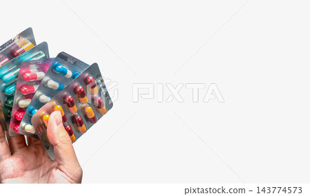 Hand holding blister packs of antibiotic capsules in yellow and burgundy, pink and white, blue and white, and green, with silver pharmaceutical packaging for antimicrobial resistance awareness. Hand holding blister packs of antibiotic capsules in yellow and burgundy, pink and white, blue and white, and green, with silver pharmaceutical packaging for antimicrobial resistance awareness. 143774573