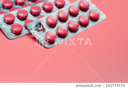 Pink round painkiller tablets in overlapping silver blister packs on a pink surface, with one empty pocket and torn foil after tablet removal, prescription medicine packaging for oral pain relief. 143774574