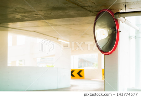 Convex safety mirror at curve of indoor car parking lot to reduce risk of accidents from blind corner or blind spots. Convex circular safety mirror in multi-level parking garage. Indoor traffic convex 143774577