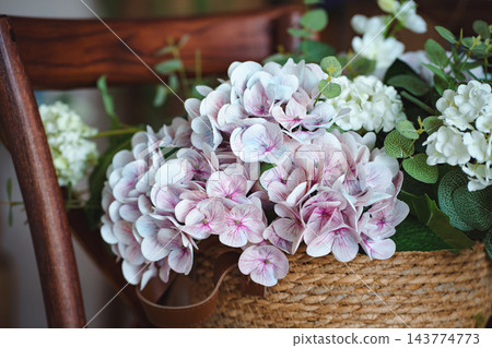 Pink and white hydrangea flowers in wicker basket on wooden chair Pink and white hydrangea flowers in wicker basket on wooden chair 143774773
