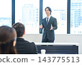 A man in a suit giving a presentation in an office conference room. 143775513