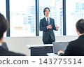 A man in a suit giving a presentation in an office conference room. 143775514