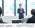A man in a suit giving a presentation in an office conference room. 143775515