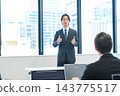 A man in a suit giving a presentation in an office conference room. 143775517