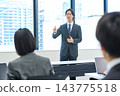 A man in a suit giving a presentation in an office conference room. 143775518