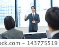 A man in a suit giving a presentation in an office conference room. 143775519