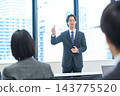 A man in a suit giving a presentation in an office conference room. 143775520