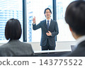 A man in a suit giving a presentation in an office conference room. 143775522