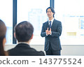 A man in a suit giving a presentation in an office conference room. 143775524