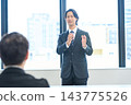 A man in a suit giving a presentation in an office conference room. 143775526