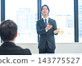 A man in a suit giving a presentation in an office conference room. 143775527
