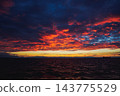 Dramatic fiery sunset over a dark ocean horizon with a cargo ship silhouette. 143775529