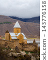 Ananuri church with conical roof and watchtower behind fortress walls and blossoming trees, Georgia 143776158