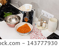 A person adds squash to a kitchen grinder while preparing squash caviar at a home kitchen counter, with a bowl, cookware, and seasonings nearby 143777930