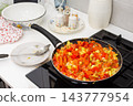 Squash and chopped vegetables cook in a pan on a kitchen stove as part of preparing squash caviar at home 143777954