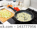 On a kitchen stove, diced onion cooks in a pan while chopped squash, carrots, and tomatoes wait on plates and a cutting board for squash caviar preparation 143777956