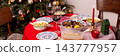 A table set for a Christmas and New Year celebration displays various dishes like salad, meat, and grains. A red candle, wine glass, and colorful decorations add to the festive atmosphere 143777957