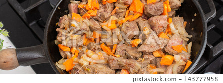 Cook prepares roast veal liver by cutting it into pieces. Nearby, there are chopped onions and carrots on a wooden board. The skillet is on the stove ready for cooking, banner Cook prepares roast veal liver by cutting it into pieces. Nearby, there are chopped onions and carrots on a wooden board. The skillet is on the stove ready for cooking, banner 143777958