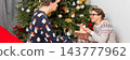 On Christmas Day, a 52-year-old couple spends time together near a decorated tree. They exchange gifts and celebrate the holiday in their cozy home setting filled with decorations 143777962