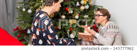 On Christmas Day, a 52-year-old couple spends time together near a decorated tree. They exchange gifts and celebrate the holiday in their cozy home setting filled with decorations 143777962