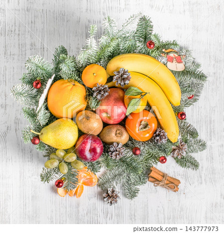 Festive arrangement of colorful fruit in a white wooden crate with evergreen branches, pinecones and cinnamon Festive arrangement of colorful fruit in a white wooden crate with evergreen branches, pinecones and cinnamon 143777973