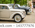 Vintage cream and black cars parked at an outdoor wedding venue, with floral accents 143777976