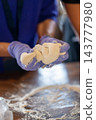 Hands kneading dough on a flour-covered wooden table during traditional food preparation. 143777980