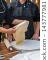 Woman preparing thin dough with a wooden rolling pin on a rustic table. 143777981