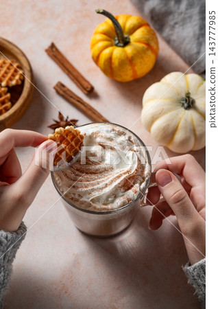 Hands in a knitted sweater hold a waffle cookies and a cup of pumpkin latte Hands in a knitted sweater hold a waffle cookies and a cup of pumpkin latte 143777985