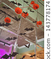 Halloween pumpkin decorations made from orange crochet yarn hang alongside black paper bats against mirrored wall. Pumpkin garland creates seasonal Background for festive design, craft projects 143778174