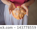 Woman holding a round pan de muerto with a raised dough bone design. 143778559