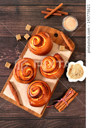 Cinnamon rolls on a wooden table, accompanied by cinnamon sticks and burnt sugar, traditional autumn and winter dessert for the cold season. Ideal as a design template or for a shop window display, Cinnamon rolls on a wooden table, accompanied by cinnamon sticks and burnt sugar, traditional autumn and winter dessert for the cold season. Ideal as a design template or for a shop window display, 143778621