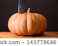 orange pumpkin on the wooden table. autumn vegetable harvest. dark background for thanksgiving or halloween carving concept. huge old knife stick in the vegetable 143778686