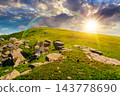 sunset over Carpathian mountain summer landscape. meadow with huge stones among the grass on top of the hillside near the peak of mountain range. dramatic sky with rainbow 143778690