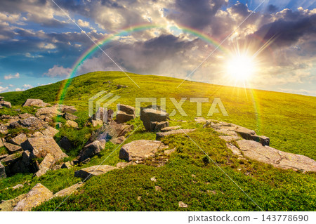 sunset over Carpathian mountain summer landscape. meadow with huge stones among the grass on top of the hillside near the peak of mountain range. dramatic sky with rainbow sunset over Carpathian mountain summer landscape. meadow with huge stones among the grass on top of the hillside near the peak of mountain range. dramatic sky with rainbow 143778690