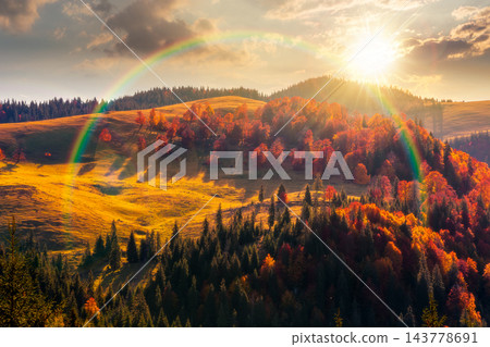 sunset over hillside of mountain range with mixed forest and alpine meadow in autumn colors. Apuseni national park under cloudy sky with rainbow. Romania in fall season 143778691