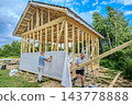 Worker fixes windproof membrane to timber frame with staple gun as structure takes shape. 143778888