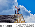 Installing corrugated asphalt roofing sheets, construction worker positions new panel beside completed section of pitched timber roof. 143778895