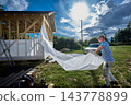 Construction wrap unrolled by builder into long sheet for covering timber frame walls with protective layer against wind and moisture. 143778899