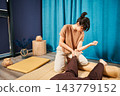 Masseuse making thai yoga massage. Woman therapist doing traditional massage treatment for female patient using elbow. Client lying on mat, meditating, enjoying hand massage in calm atmosphere. 143779152